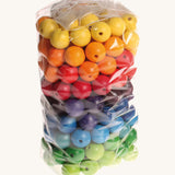 Rainbow coloured wooden Grimms beads in bag on a cream background.