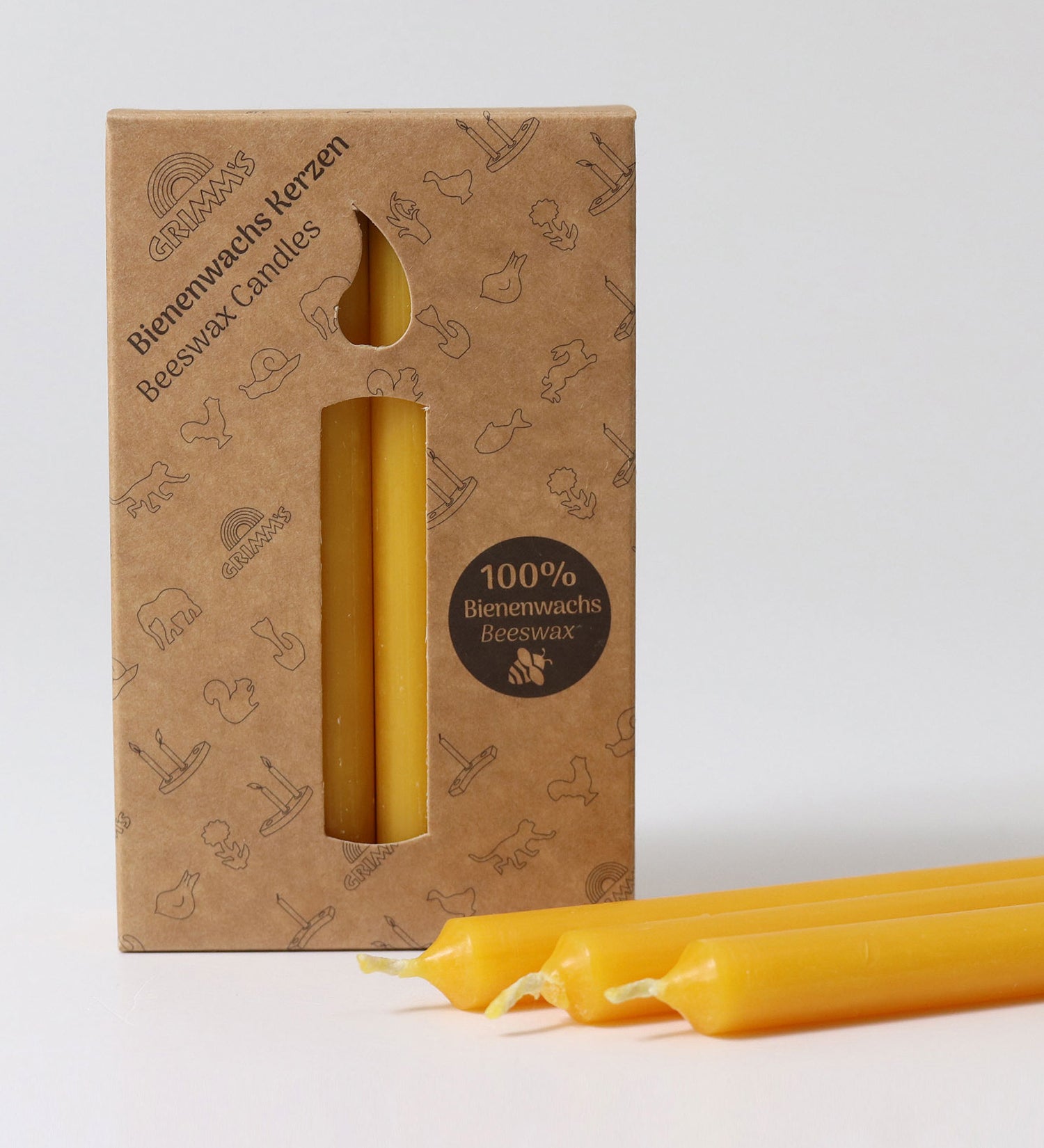 A pack of 12 Grimm's amber 100% beeswax candles in a cardboard box with three candles at the front laid out in front of the box.