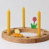 Grimm's Amber beeswax candles placed on a natural celebration ring with a pink flower and bee wooden decorative figures.