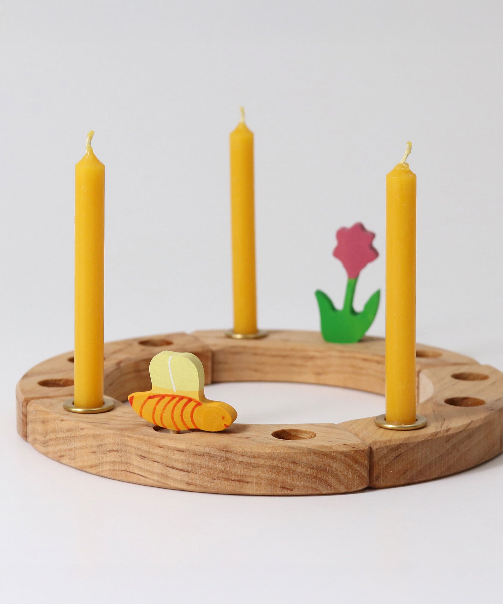 Grimm's Amber beeswax candles placed on a natural celebration ring with a pink flower and bee wooden decorative figures.