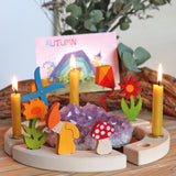 A Autumn display with the Grimms celebration ring with different wooden decorative figures on top including a kite, windmill, flowers, Autumn dwarf, mushroom and beeswax candles