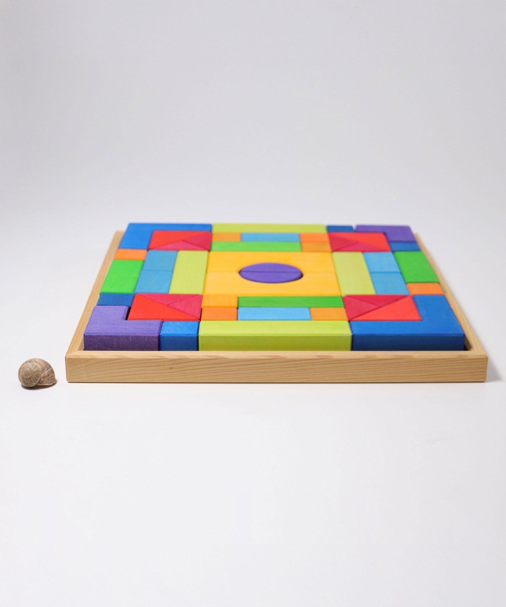 The Grimm's Basic Building Set 2 wooden block set shown in it's wooden storage tray next to a snail's shell.