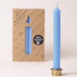 A blue Grimm's beeswax candle in a metal stand, with a packet of candles in the background.
