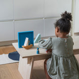 A child playing with the Grimm's blue boat Wooden Stacking Puzzle. The child has the blocks placed in a boat shape and has placing Grimm's friends wooden peg dolls on the boat. These Grimm's toys are part of a wide range of wooden toys available here at Babipur.