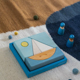 A Grimm's blue boat Wooden Stacking Puzzle placed on a rug. These Grimm's toys are part of a wide range of wooden toys available here at Babipur.