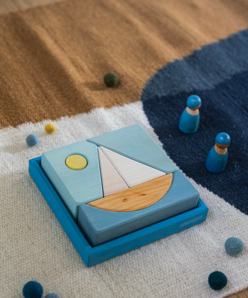 A Grimm's blue boat Wooden Stacking Puzzle placed on a rug. These Grimm's toys are part of a wide range of wooden toys available here at Babipur.