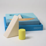 The white triangle and green cylinder wooden block from the Grimm's blue building set placed in front of the blue tray. These Grimm's wooden block sets are part of a wide range of wooden toys available here at Babipur.