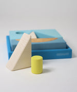 The white triangle and green cylinder wooden block from the Grimm's blue building set placed in front of the blue tray. These Grimm's wooden block sets are part of a wide range of wooden toys available here at Babipur.