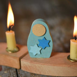 A Grimm's Matryoshka Stars Decorative Figure placed in between two lit candles on a natural celebration ring.