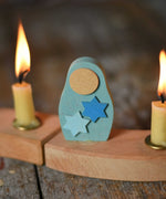 A Grimm's Matryoshka Stars Decorative Figure placed in between two lit candles on a natural celebration ring.
