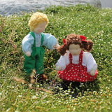 Grimm's Brown Haired Girl Doll - Lana is sat on a flowery patch of grass with another Grimm's Waldorf Doll - Linde, handmade, fabric doll next to it