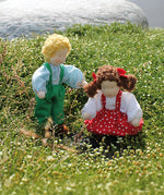 Grimm's Brown Haired Girl Doll - Lana is sat on a flowery patch of grass with another Grimm's Waldorf Doll - Linde, handmade, fabric doll next to it