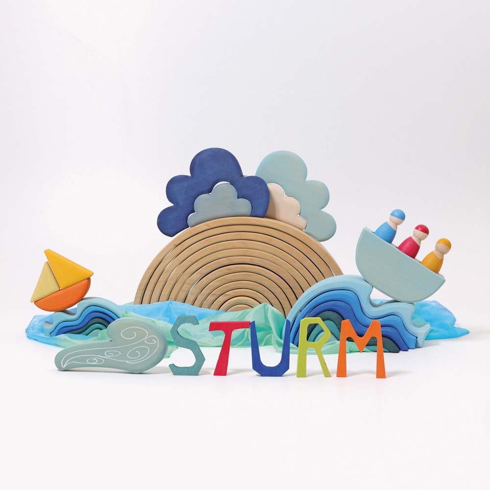 The Grimm's Wooden Weather Building Set set up along side the 12 piece natural rainbow and free standing letters, waves and Grimm's boat with 3 friends. The scene depicts a storm.