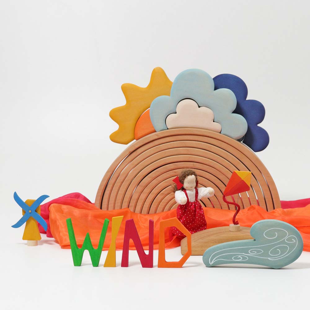 The Grimm's Wooden Weather Building Set set up along side the 12 piece natural rainbow and free standing letters. The scene depicts a windy day.