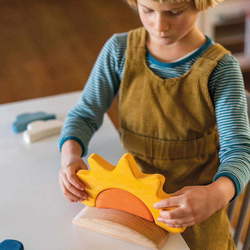 A child placing the sun piece from the Grimm's weather set on the wooden base piece.