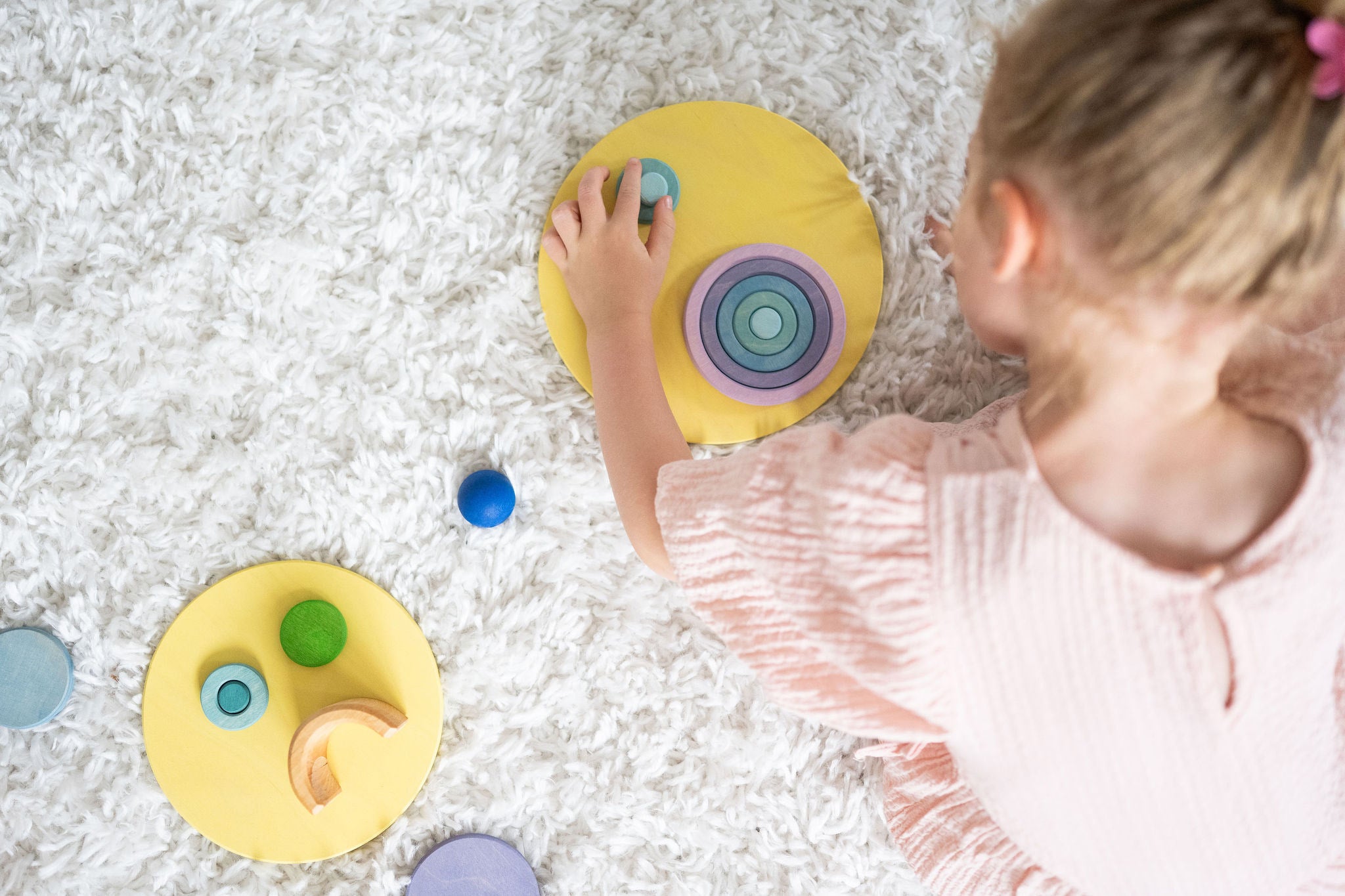 A top view of a child creating faces and abstract shapes with the Grimm's concentric wooden rings and circles