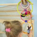 A child has ties some of the Grimm's wooden rings together to create a cascading chain, and she hangs peg dolls on them in a small world play scene