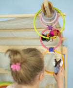 A child has ties some of the Grimm's wooden rings together to create a cascading chain, and she hangs peg dolls on them in a small world play scene