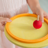 A little girl spinning a Grimm's wooden spinning top on one of the concentric circles