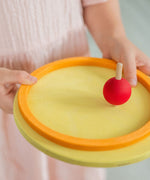 A little girl spinning a Grimm's wooden spinning top on one of the concentric circles
