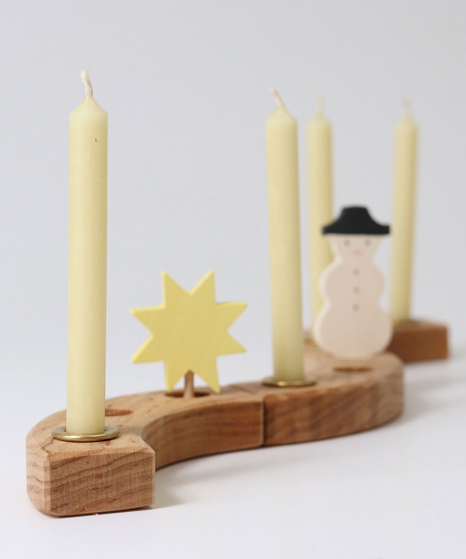 Grimms 100% beeswax candles in brass candle holders slotted in pieces from the decorative ring with a star and snowman figure creating a festive display