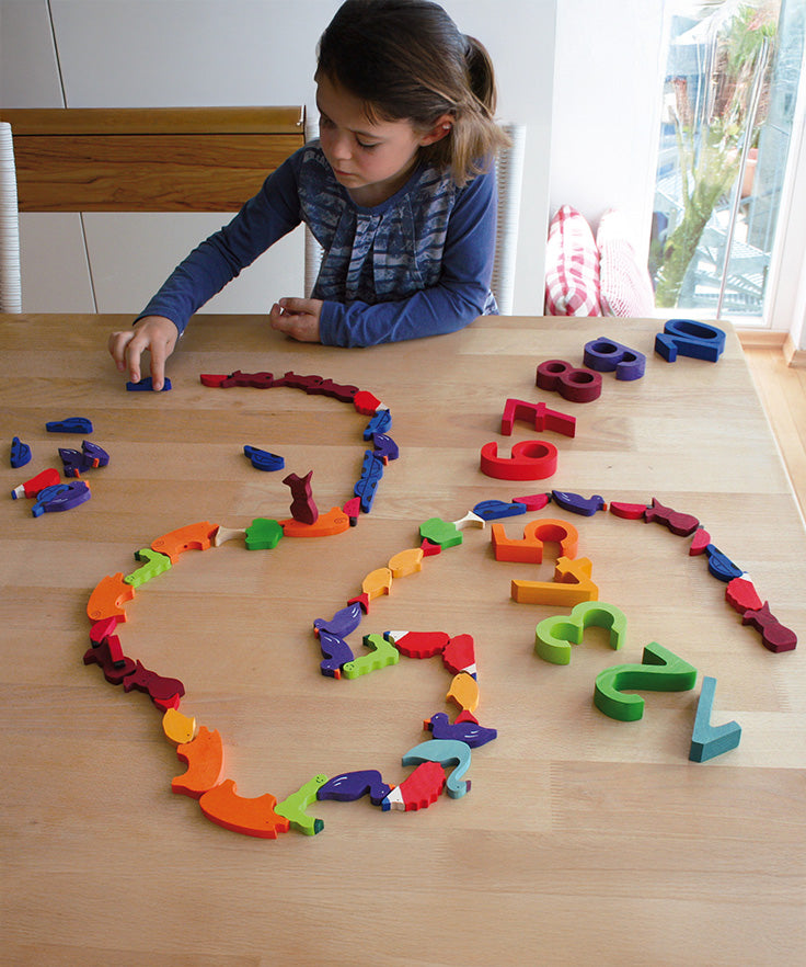 A child playing with the Grimm's Figures For Counting & Story Telling on a wooden table.