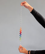 An adult holding each end of the giant Grimms spirelli available at Babipur. This  winding metal wire comes with coloured  wooden disks that make a noise when tipped over.