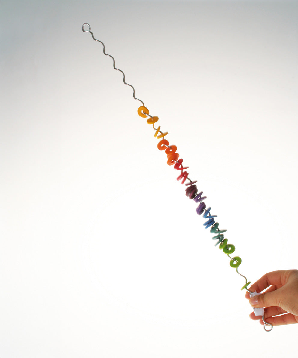 An adult holding one end of the giant Grimms spirelli available at Babipur. This  winding metal wire comes with coloured disks that make a noise when tipped over.