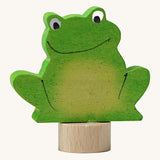 A Grimms green frog wooden decorative figure with playful features and a small base stand to slot into a decorative ring