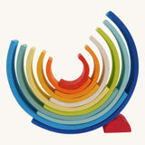 The Grimm's Gwawr Sunrise 12 Piece Rainbow on a plain background. The pieces have been placed in an upturned position with the smallest red pieced helping the structure balance.