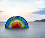 A Grimm's Gwawr Sunrise 12 Piece Rainbow placed on the sand on a beach.
