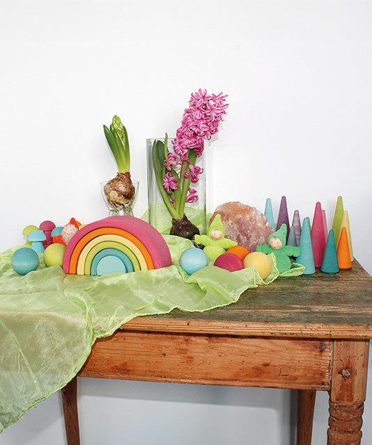A Grimm's Medium Pastel Rainbow (6 Pieces) on a sideboard with other wooden Grimm's items including wooden balls, forest, mushrooms and gnomes.