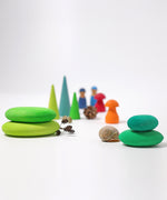 The Grimm's moss green wooden pebbles shown alongside a snail shell and nature finds with other Grimms wooden toys seen in the background.