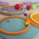 Pastel rainbow Grimm's stacking toys arranged with wooden balls on top, highlighting creative floor play and colour matching.