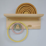 Grimm's wooden rings displayed on a wall peg and shelf, showing neat and accessible toy storage for Montessori or Waldorf playrooms.