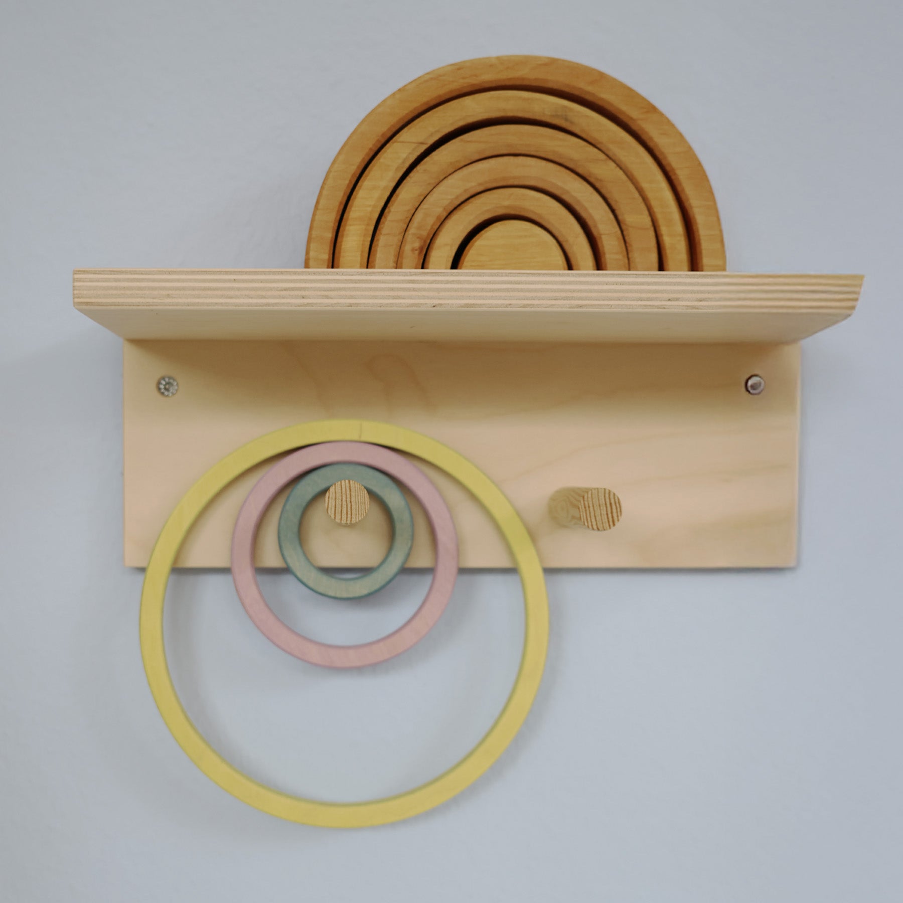 Grimm's wooden rings displayed on a wall peg and shelf, showing neat and accessible toy storage for Montessori or Waldorf playrooms.