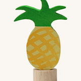 A Grimms pineapple wooden decorative figure with green leaves and a small base stand to slot into a decorative ring