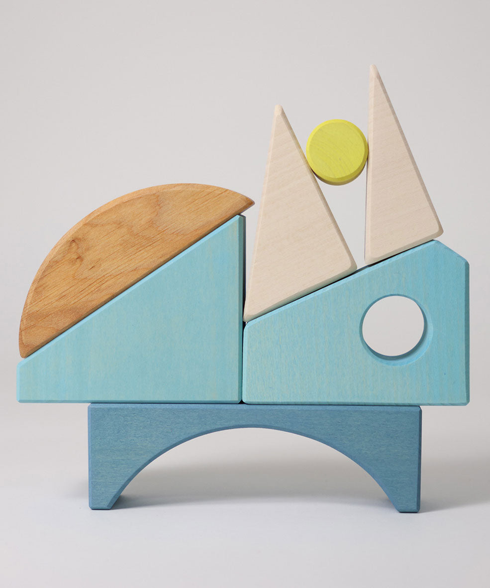 The wooden blocks from the Grimm's Building Set in Blue stacked up on top of each other. A set of wooden blocks that form a sailing boat when placed in the blue coloured storage tray.