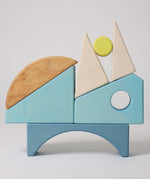 The wooden blocks from the Grimm's Building Set in Blue stacked up on top of each other. A set of wooden blocks that form a sailing boat when placed in the blue coloured storage tray.