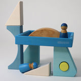 The blocks from the Grimm's Building Set Blue used in a small world play scene with two Grimm's friends wooden peg dolls. These Grimm's wooden block sets are part of a wide range of wooden toys available here at Babipur.