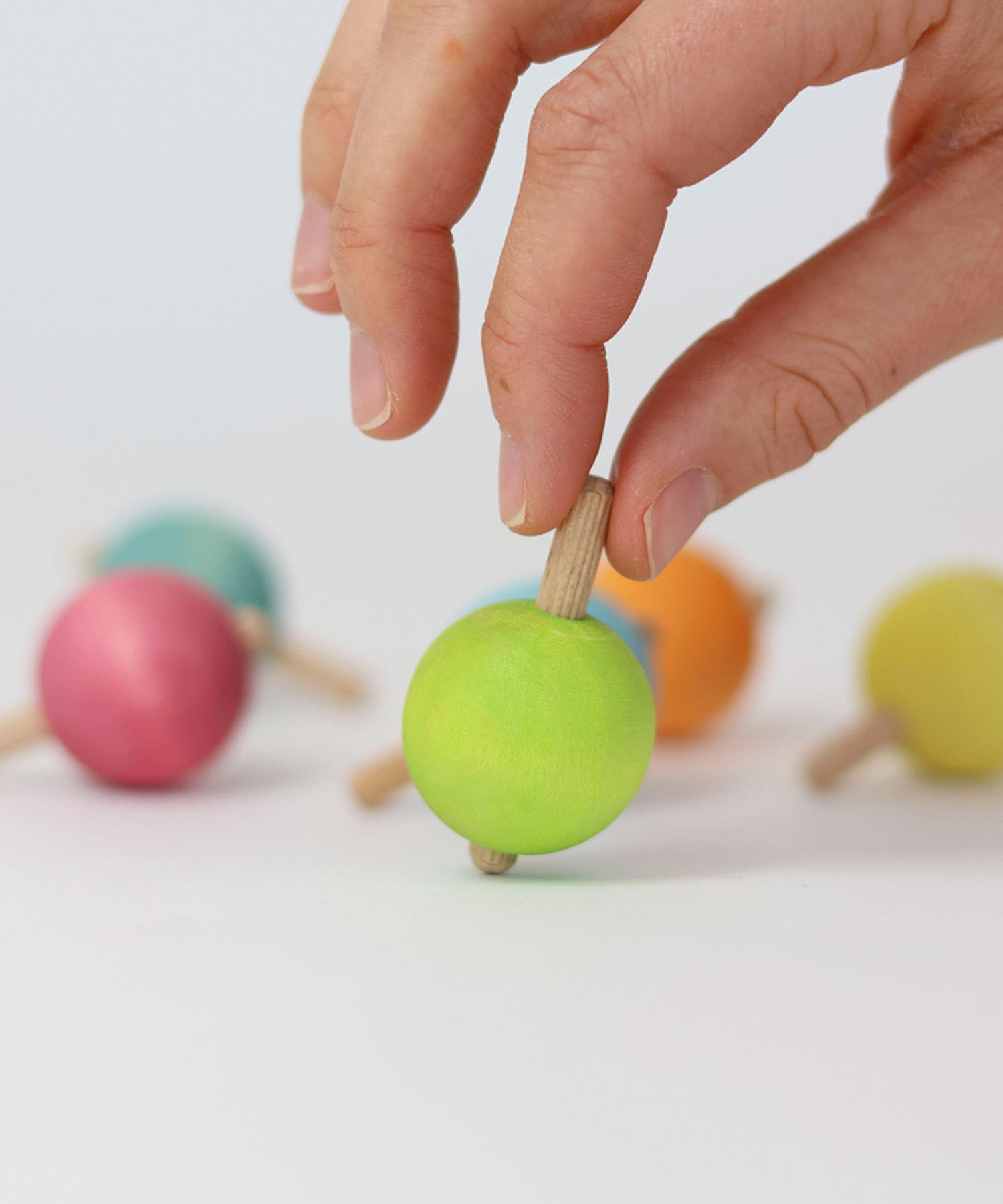 A hand ready to spin the green pastel wooden spinning top from Grimm's.