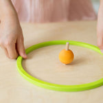 A child has arranged the yellow pastel wooden spinning top from Grimm's inside the green concentric ring.