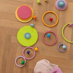 The Grimm's wooden concentric pastel rainbow rings and circles laid out on the floor, along with the rainbow and pastel wooden spinning tops.