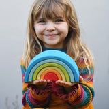 A child holding the Grimm's Babi Gwawr Sunrise 6 Piece Rainbow in their hands.