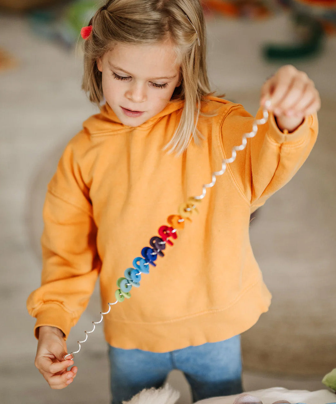 An toddler holding each end of the giant Grimms spirelli available at Babipur with the coloured disks threading through the metal wire