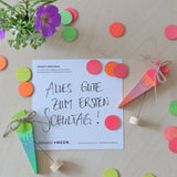 A flatlay of the green and pink neon birthday cone decorative figures next to the mixed neon confetti dots on a wooden surface.