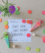 A flatlay of the green and pink neon birthday cone decorative figures next to the mixed neon confetti dots on a wooden surface.