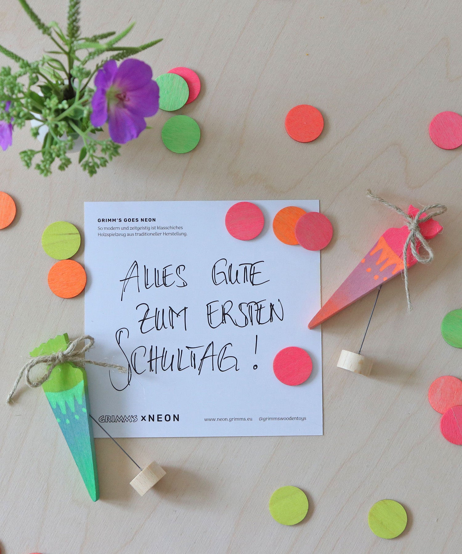 A flatlay of the green and pink neon birthday cone decorative figures next to the mixed neon confetti dots on a wooden surface.