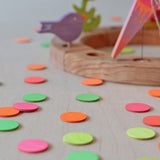A close of the Grimm's Neon Confetti Dots scattered next to a celebration ring with a singing birds and neon pink cone sitting on top of the ring