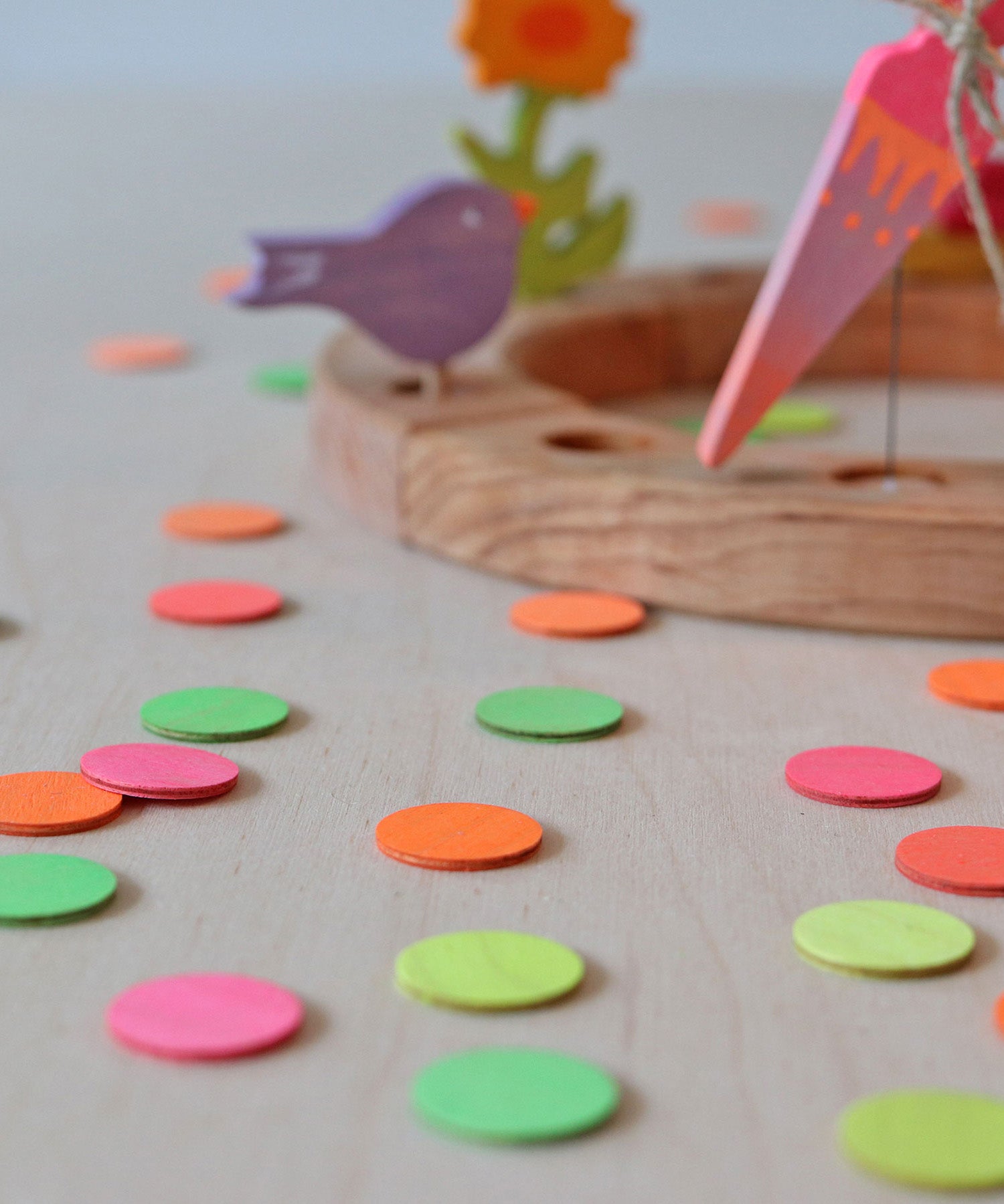 A close of the Grimm's Neon Confetti Dots scattered next to a celebration ring with a singing birds and neon pink cone sitting on top of the ring